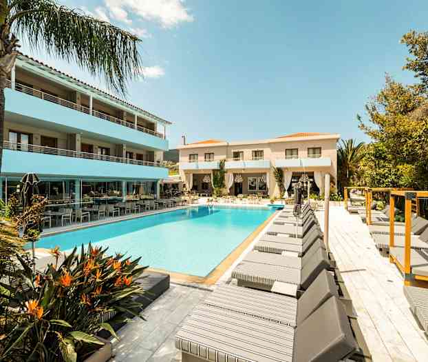 En hotellpool omgiven av solstolar och byggnader under en klarblå himmel. (AI-genererad text)