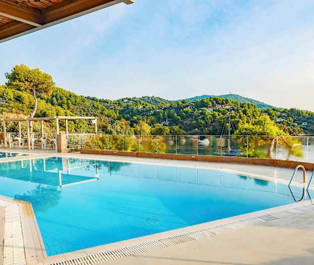 Ett utomhuspoolområde med utsikt över gröna kullar och en lugn sjö. (AI-genererad text)