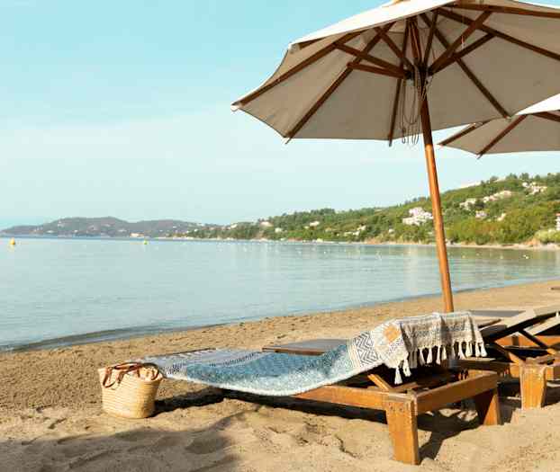 Strand med solstolar och stora parasoller samt havsutsikt. (AI-genererad text)