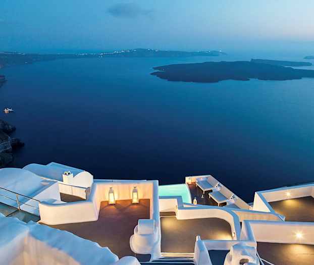 En vy vid skymning med vita byggnader nära vatten och berg. (AI-genererad text)