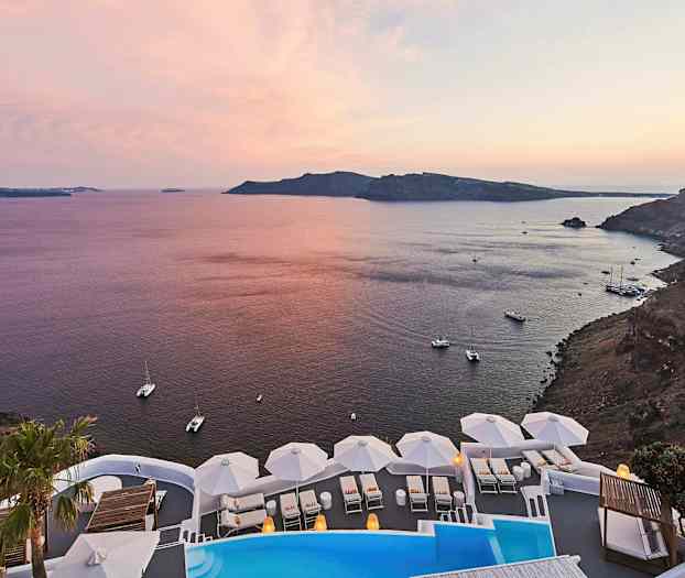 En vy över en kustlinje med utsikt över havet vid solnedgången. I förgrunden syns en pool och vita solstolar med parasoller. (AI-genererad text)