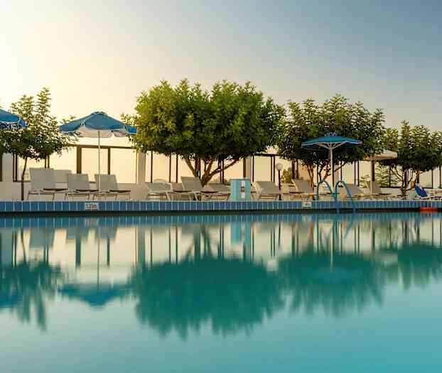 Utomhuspool med omgivande träd, parasoller och solstolar. (AI-genererad text)