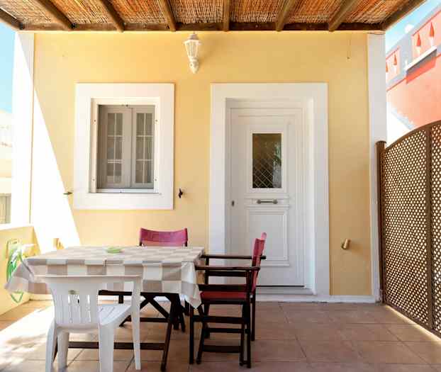 En uteplats med ett bord och stolar framför en dörr och ett fönster. (AI-genererad text)