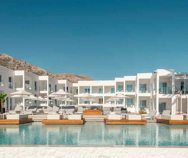 Vit hotellbyggnad med utomhuspool och solstolar. (AI-genererad text)