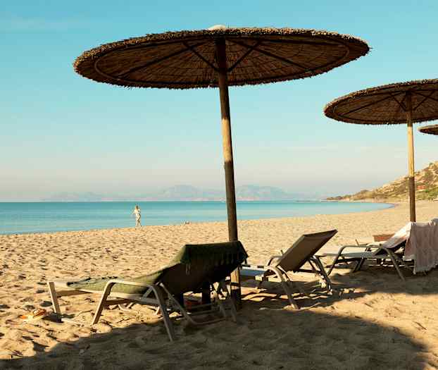 En sandstrand med parasoller och solstolar vid havet. (AI-genererad text)