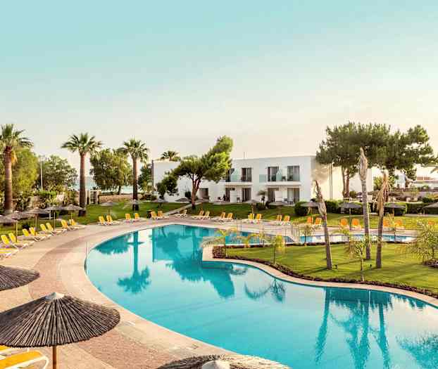 Stor pool omgiven av solstolar och parasoller, med gröna gräsmattor och palmer i bakgrunden samt vita byggnader. (AI-genererad text)