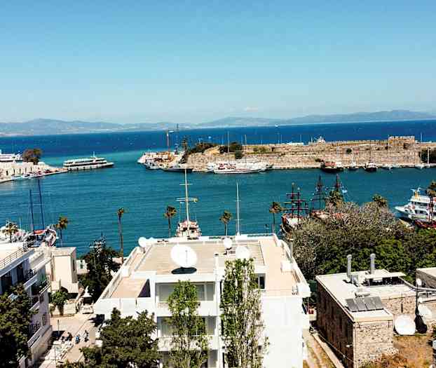 Vy över ett hamnområde med båtar och en historisk byggnad vid kusten. (AI-genererad text)