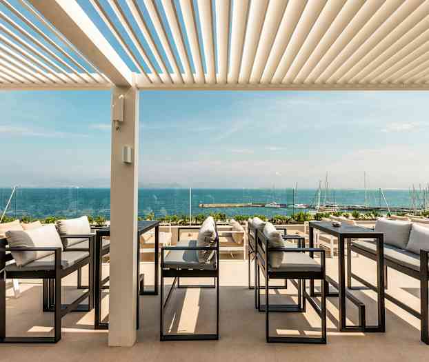 Uteservering med utsikt över havet, med soffor och bord under en pergola. (AI-genererad text)