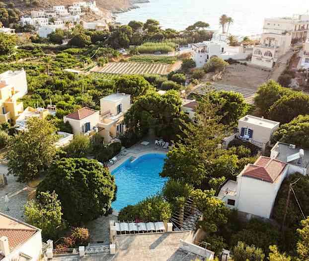 Vy över en pool omgiven av grönska och hus i ett soligt område. (AI-genererad text)