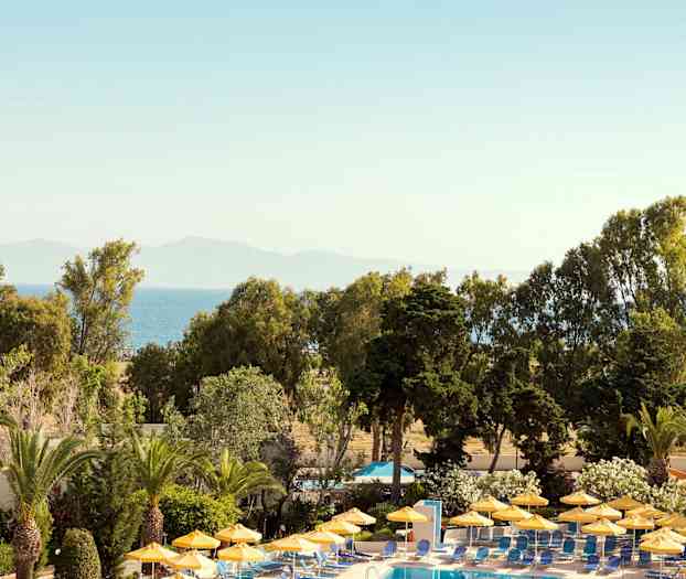 Poolområde med gula parasoller omgiven av grönska och med utsikt över havet. (AI-genererad text)