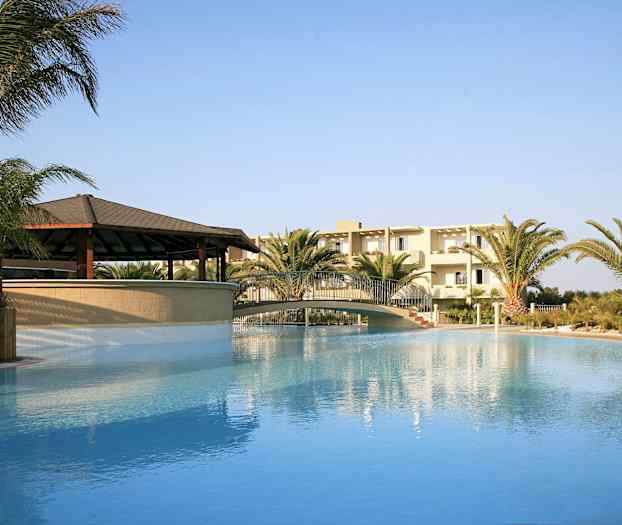 Utomhuspool med bro, omgiven av palmer och en byggnad i bakgrunden. (AI-genererad text)