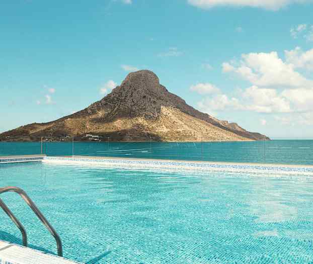 En pool med klart blått vatten framför ett berg vid havet under en klar himmel. (AI-genererad text)