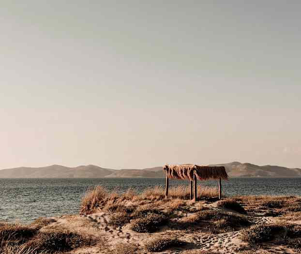 Ett strandlandskap med ett enkelt skydd av trä och halm vid havet. (AI-genererad text)