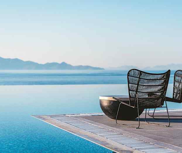 Två stolar vid kanten av en infinitypool med hav och berg i bakgrunden. (AI-genererad text)