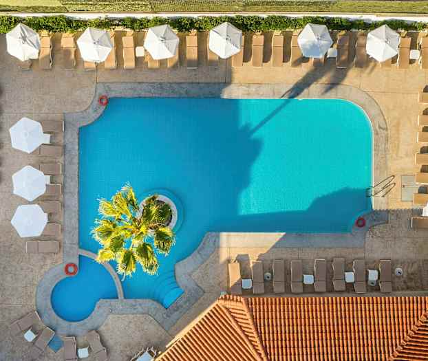 En fågelperspektivvy av en rektangulär pool med solstolar och parasoller runt omkring. (AI-genererad text)