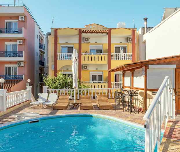 Byggnader med balkonger och en pool med solstolar i förgrunden. (AI-genererad text)