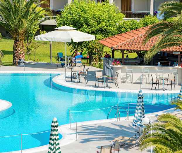 En utomhuspool med omgivande solstolar, parasoller och en poolbar under ett tak med röda takpannor. (AI-genererad text)