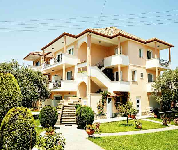 Ett bostadshus med flera våningar, balkonger och en välskött trädgård med gröna buskar. (AI-genererad text)