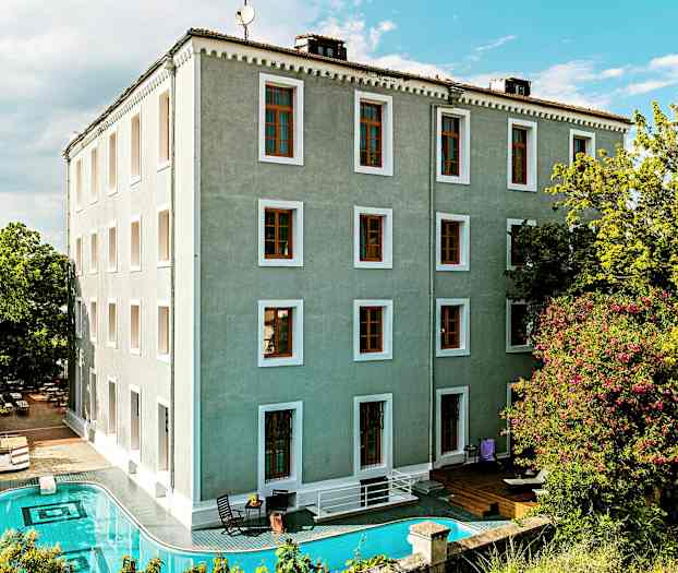 Byggnad med grönt fasad med en pool framför och omgivande grönska. (AI-genererad text)