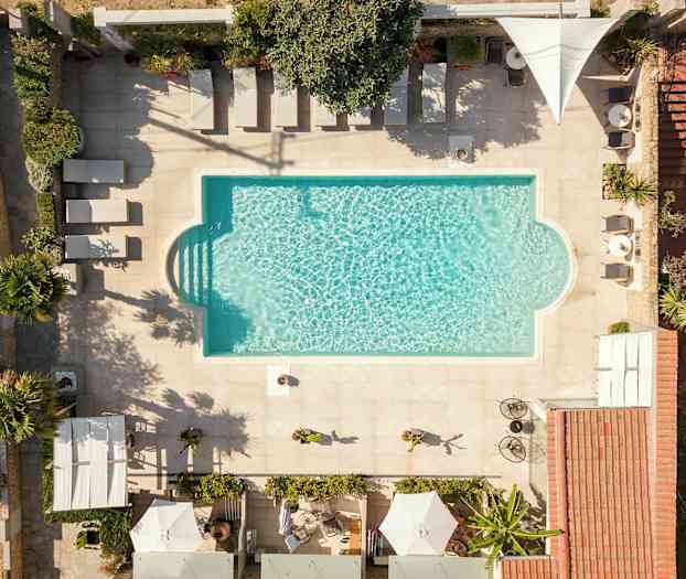 En utomhuspool med parasoller och solsängar med omkringliggande växtlighet. (AI-genererad text)