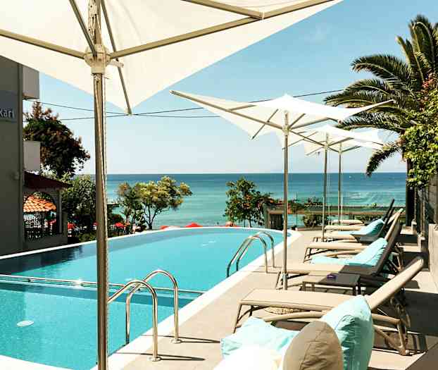 Poolområde med solstolar och parasoller samt havsutsikt. (AI-genererad text)