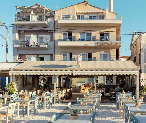 Uteservering med bord och stolar framför en hotellbyggnad. (AI-genererad text)