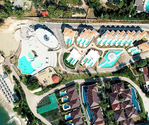Flygfoto av ett badortsområde med pooler, byggnader och strand. (AI-genererad text)