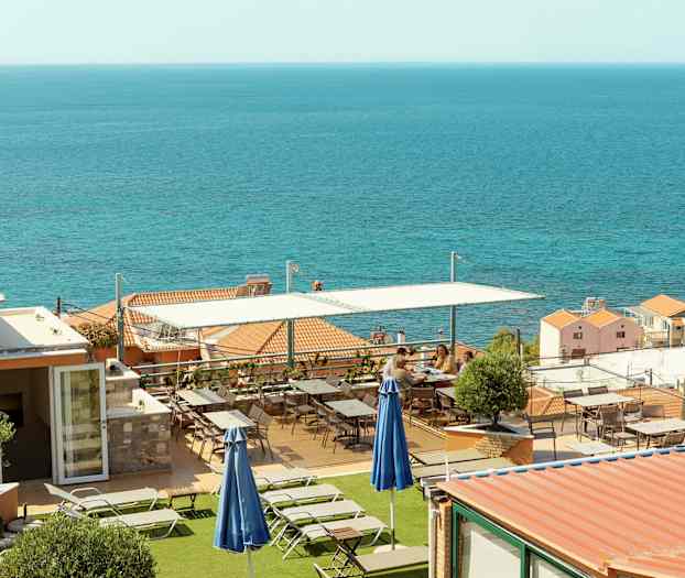 Terrass med solstolar och bord, med havet i bakgrunden. (AI-genererad text)