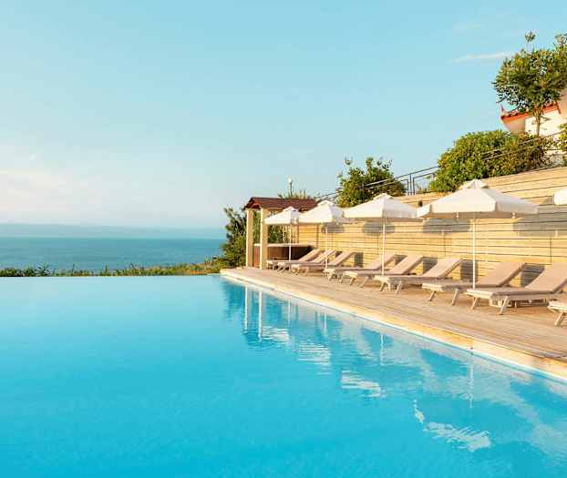 Utsikt över en infinitypool med solstolar och parasoller vid sidan. (AI-genererad text)