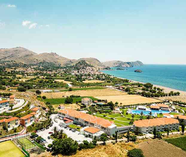 Flygfoto av ett kustlandskap med hotellbyggnader, grönområden och havet i bakgrunden. (AI-genererad text)