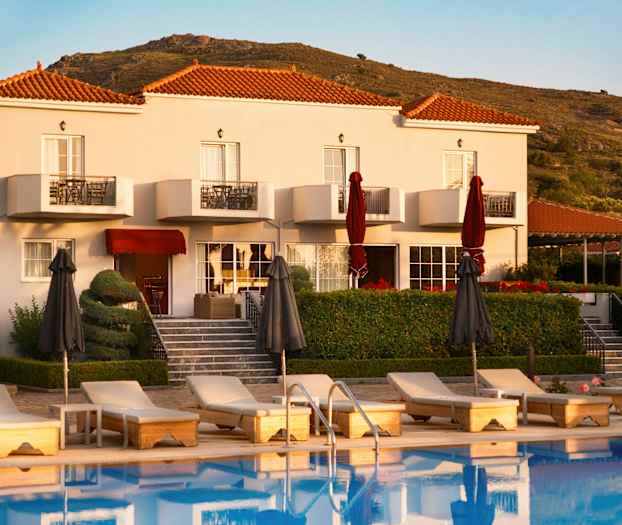 Hotellbyggnad med pool och solstolar framför samt omgivande kullar. (AI-genererad text)