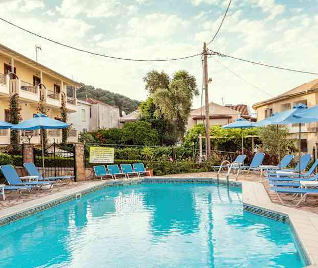 En pool omgiven av solstolar och parasoller, med byggnader och träd i bakgrunden. (AI-genererad text)