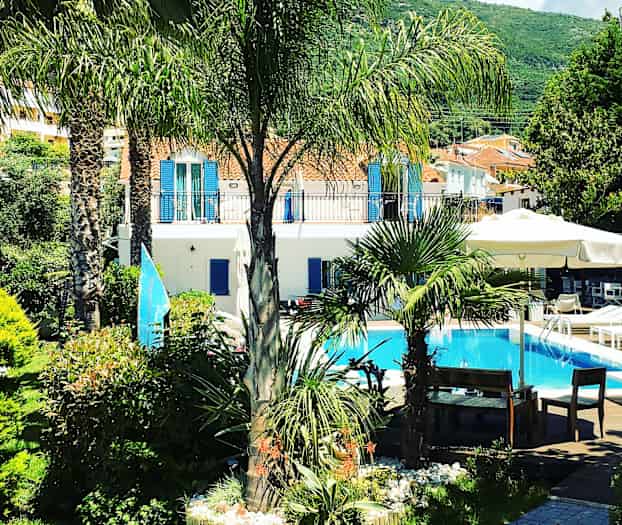 En trädgård med palmer och växter kring en pool framför en ljus byggnad. (AI-genererad text)