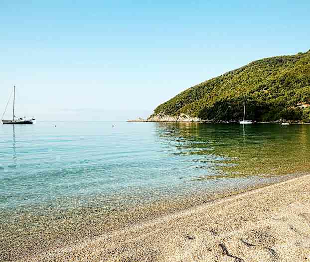 En lugn strand med klart vatten och segelbåtar i fjärran. (AI-genererad text)