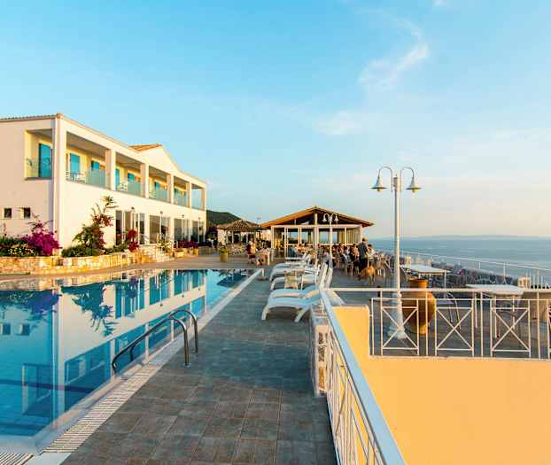 En hotellbyggnad vid en utomhuspool och en sittgrupp med utsikt över havet. (AI-genererad text)