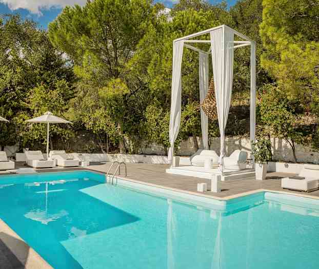 Swimmingpool med omgivande vita solstolar och parasoller samt grönskande träd i bakgrunden. (AI-genererad text)