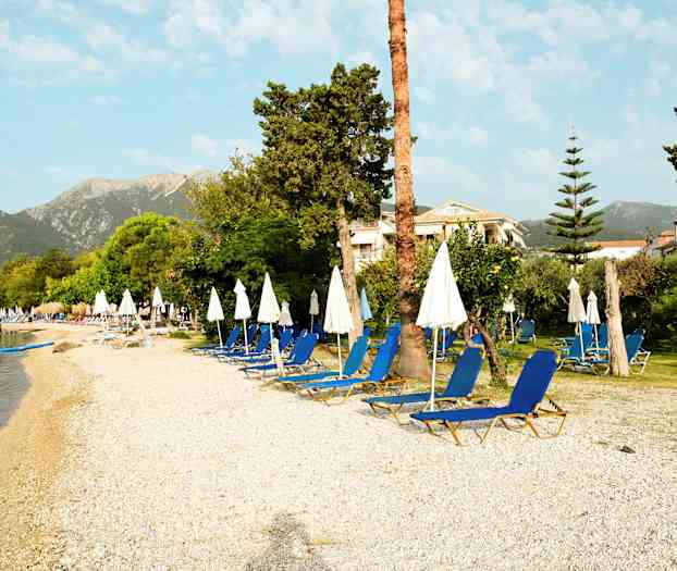 En strand med solstolar och parasoll, omgiven av grönska och byggnader i bakgrunden. (AI-genererad text)