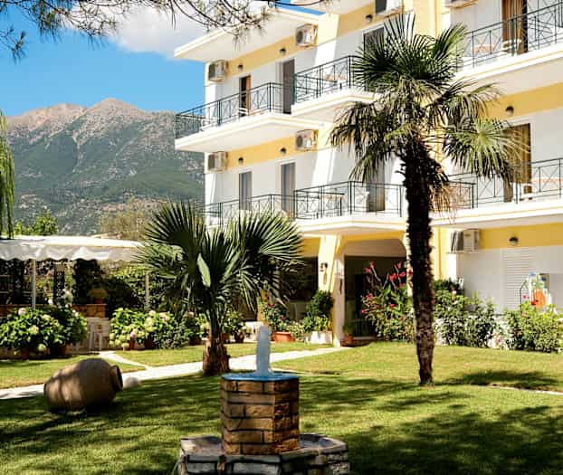 Hotellets trädgård med grönska, en fontän och byggnaden i bakgrunden. (AI-genererad text)