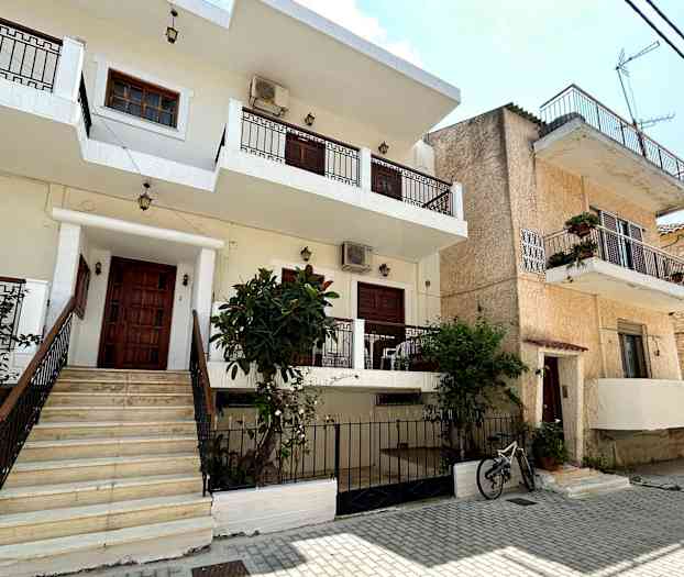 En byggnad i flera våningar med balkonger och trädgård inför en stenlagd gata. (AI-genererad text)