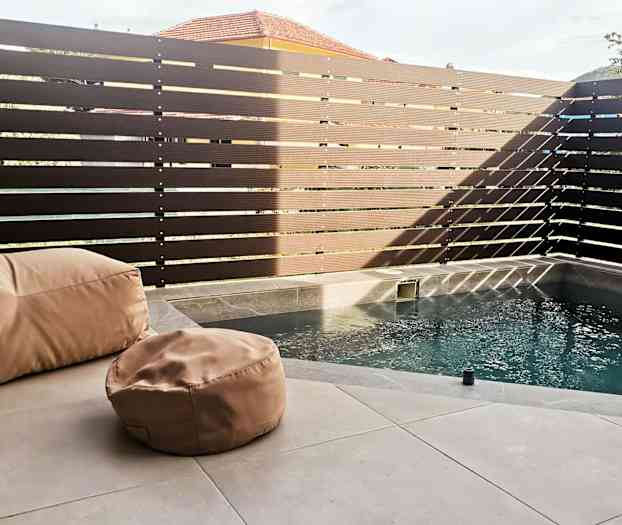 Liten pool med beige sittsäckar på en stenyta, omgiven av ett högt, mörkt staket. (AI-genererad text)