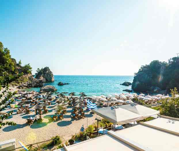 Sandstrand med parasoller och solstolar vid klarblått hav, omgiven av klippor och grönska. (AI-genererad text)