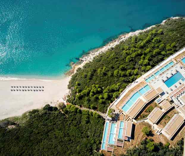 Flygfoto av en strand vid havet, omgiven av skog och ett semesterkomplex. (AI-genererad text)