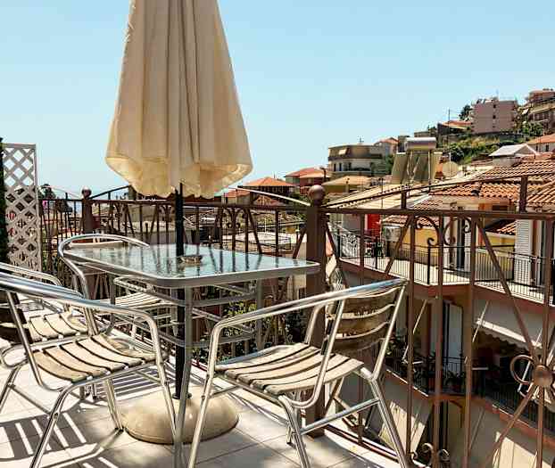 En terrass med ett bord, stolar och parasoll, med utsikt över hus med tegeltak. (AI-genererad text)