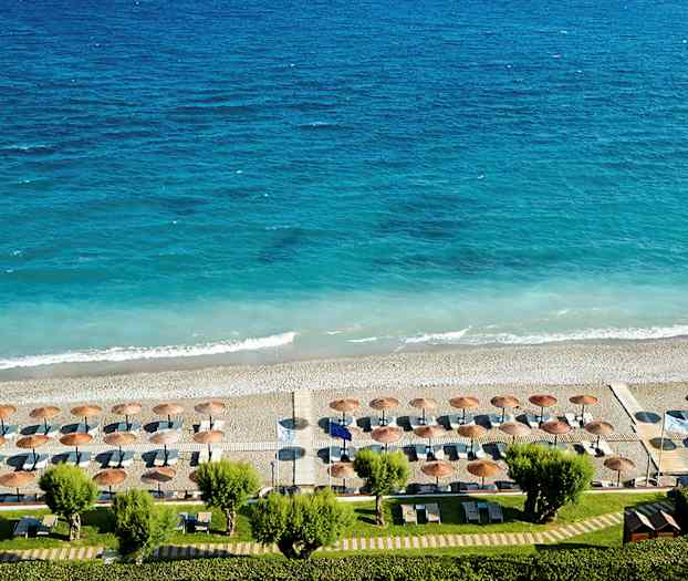 Utsikt över en strand med parasoller och solstolar mot ett blått hav. (AI-genererad text)