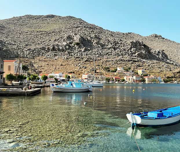 En hamn med klart vatten, små båtar och färgglada hus vid foten av steniga berg. (AI-genererad text)