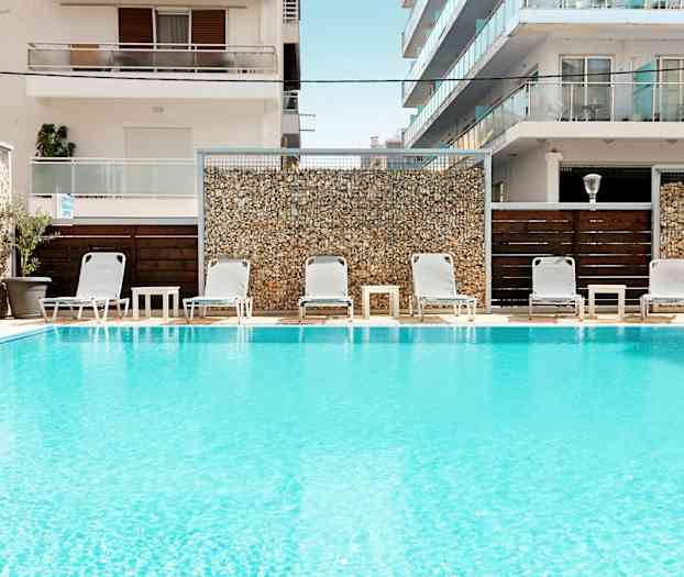 Pool med solstolar och bord framför byggnader. (AI-genererad text)