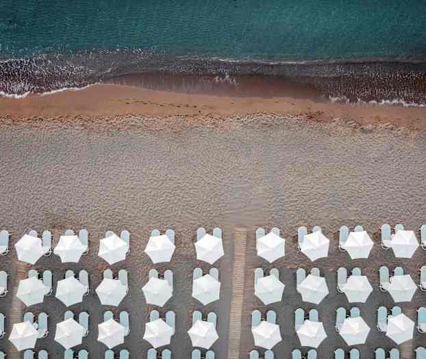 Fågelspråksperspektiv av strand med vita parasoller och solstolar vid kanten av havet. (AI-genererad text)