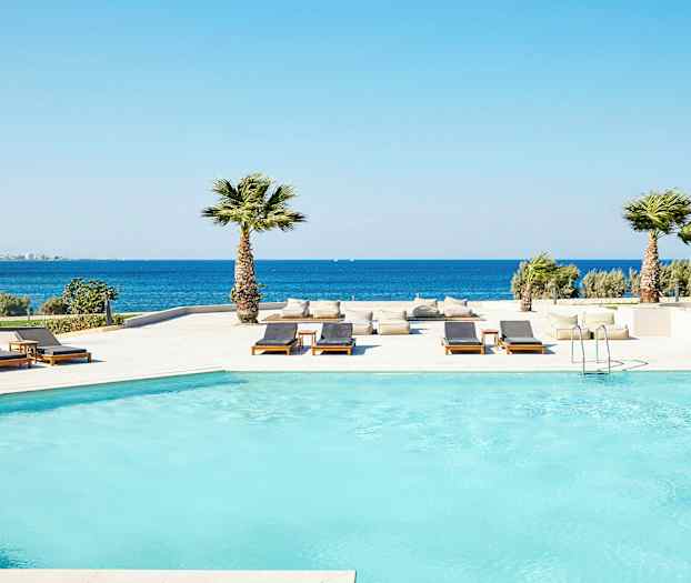 Poolområde vid havet med solstolar och palmer. (AI-genererad text)