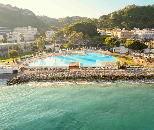 En stor pool vid havet, omgiven av byggnader och grönska. (AI-genererad text)