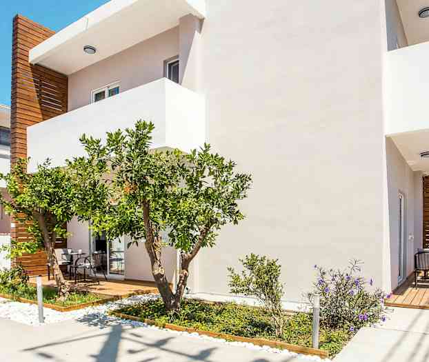 Vit byggnad med trädetaljer, en terrass och grönskande trädgård. (AI-genererad text)